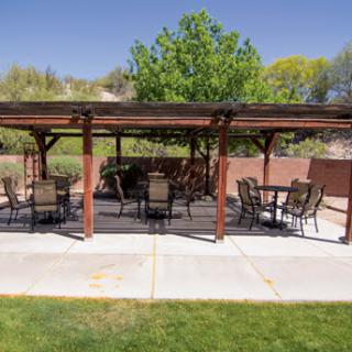 A serene outdoor patio under a pergola, featuring seating arrangements surrounded by lush greenery.