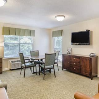 A well-lit living room with a dining table, chairs, and a television mounted on the wall.