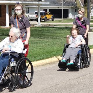 Caregivers assisting elderly individuals in wheelchairs during an outdoor walk.