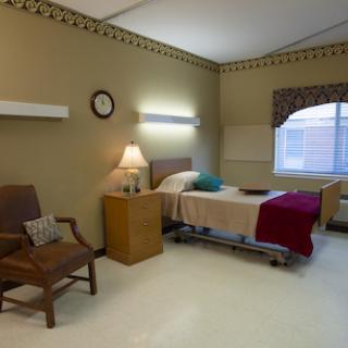 A calm and clean hospital room featuring a bed, bedside table with a lamp, and a comfortable chair.