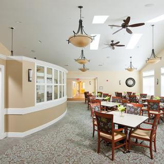 A spacious dining area with multiple tables and chairs, featuring hanging lighting fixtures, ceiling fans, and skylights.