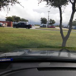 A view from inside a vehicle facing a grassy area with trees and a cloudy sky.