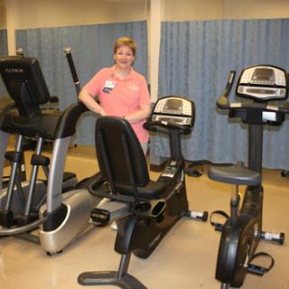 A fitness trainer standing beside various exercise machines in a gym setting.