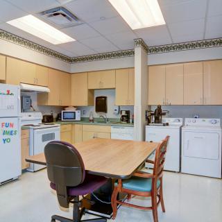 A kitchen area with various appliances and a central table with chairs.