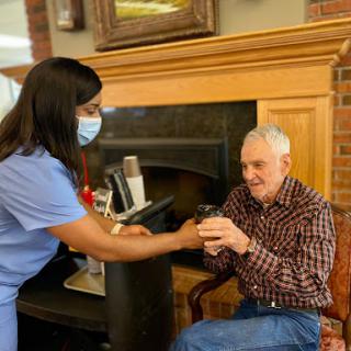 A caregiver assists an elderly man in a warm, indoor setting.