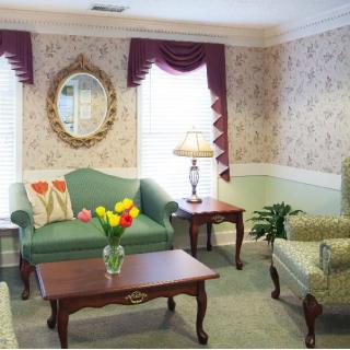 A cozy living room with classic decor, including a green sofa, patterned armchairs, and a wooden coffee table adorned with a vase of flowers.