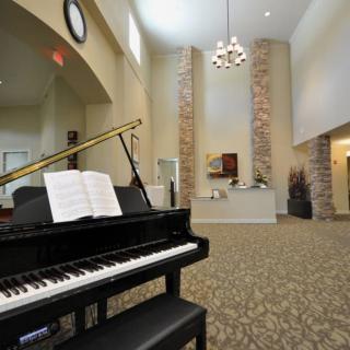 A spacious lobby featuring a grand piano under a chandelier and high ceilings.