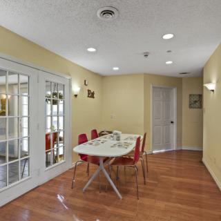 A modern dining room with a sleek table and vibrant red chairs, featuring wood flooring and glass doors.