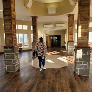 A woman walks through a spacious, well-lit lobby with wooden floors and architectural columns.