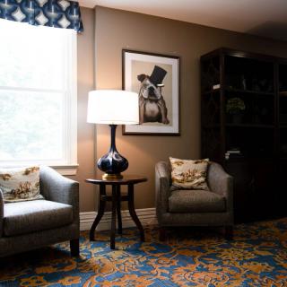 A cozy living room with two armchairs, a lamp on a small table, and artwork on the wall.