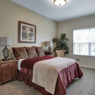 A cozy bedroom with a plush bed, decorative pillows, and a large window allowing natural light to fill the space.