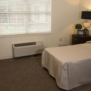 A cozy bedroom with a bed, side table, lamp, and an air conditioner beneath the window.