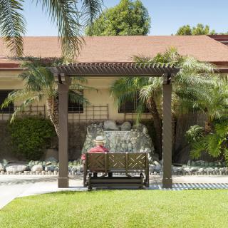 A serene garden scene featuring a bench under a pergola surrounded by lush greenery and a paved pathway.