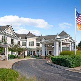 A large residential building with a prominent entrance and well-maintained landscaping, featuring an American flag.