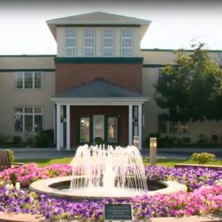 A building with a fountain surrounded by colorful flowers in front.
