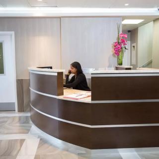 A receptionist sitting at a modern reception desk with flowers in an office lobby.