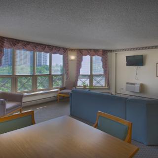A cozy living room with a large window, seating area, and a wall-mounted TV.