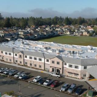 Aerial view of a large building with a parking lot in front, surrounded by a residential neighborhood and trees.