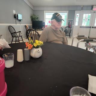 An elderly man sitting at a dining table with decorative flowers.