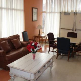 A cozy living room with a leather sofa, coffee table, and chairs, softly lit by natural light through the curtains.