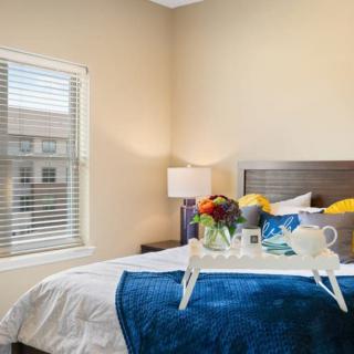 A cozy bedroom with a neatly made bed, featuring a decorative tray with flowers and tea set, illuminated by a bedside lamp.