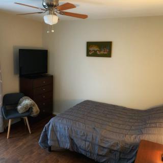 A cozy bedroom featuring a bed, television, dresser, and chair with a ceiling fan overhead.