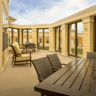 A spacious patio with outdoor seating and tables, surrounded by large windows on a sunny day.