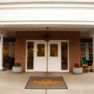 The main entrance of a building features double doors with a welcome mat and rocking chairs on either side.
