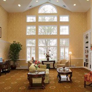 A spacious living room with large windows, elegant furniture, and a high ceiling.