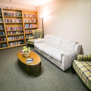 A cozy living room with a bookshelf, sofa, and chairs surrounding a coffee table.