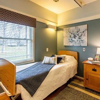 A cozy single-bed room with a nightstand, lamp, and artwork on the wall.