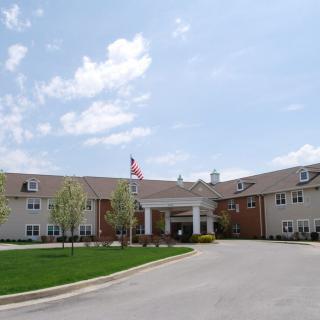 A large building with an entrance, surrounded by a parking lot and green lawn under a partly cloudy sky.