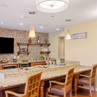 A modern kitchen interior with a spacious countertop and wooden chairs, featuring decorative shelves and stylish lighting.