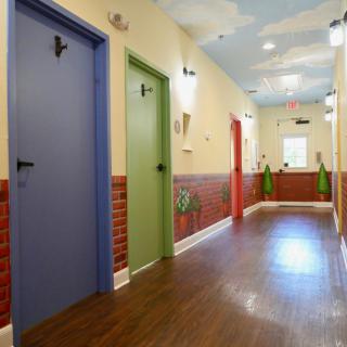 A colorful hallway with blue, green, and red doors, decorated walls, and a wooden floor.
