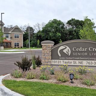 Entrance sign to Cedar Creek Senior Living with a landscaped area and building in the background.