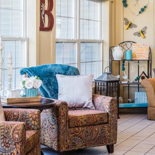 A cozy living room filled with patterned armchairs, decorative plants, and warm natural lighting.