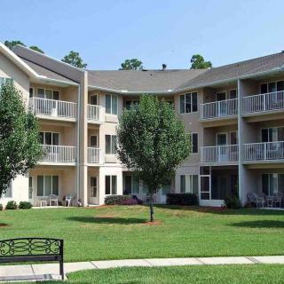 A multi-story apartment building with balconies and a well-maintained lawn featuring a park bench.