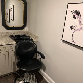 A cozy corner of a hair salon featuring a stylish chair, a mirror, and wall art.