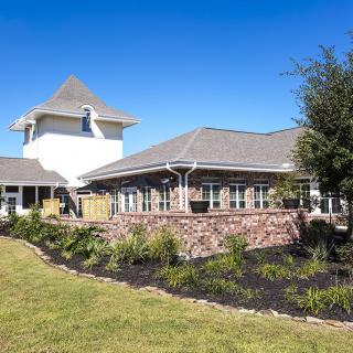 A picturesque building with a tower and landscaped garden under a clear blue sky.