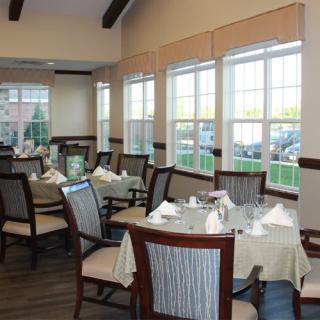 A well-lit dining room with neatly arranged tables and chairs, featuring large windows.