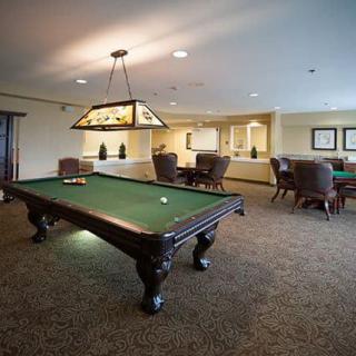 A billiard room with a pool table and seating area, elegantly lit by overhead lighting.
