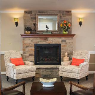 A cozy living room with a stone fireplace flanked by two armchairs and decorated with a mirror and flowers.