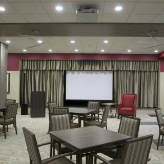 A conference room with tables and chairs, featuring a projector screen and curtains.