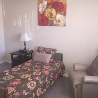A cozy bedroom featuring a single bed with floral patterned bedding, accompanied by a lamp and a stylish armchair.
