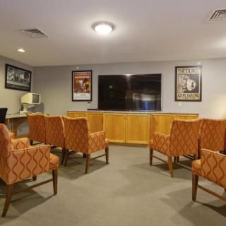 A cozy seating area with orange-patterned chairs facing a large television, adorned with film posters on the walls.