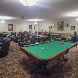 A cozy game room features a pool table surrounded by plush reclining chairs and decorated walls.