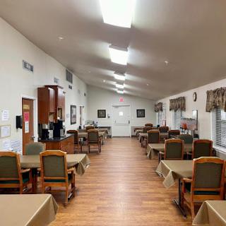A spacious dining area featuring neatly arranged tables and chairs, illuminated by bright overhead lights.