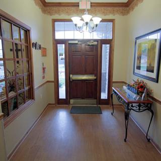 A warmly lit entrance hallway with a wooden door, chandelier, decorative table, and wall art.