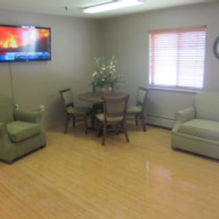 A cozy sitting area featuring comfortable green chairs, a dining table with chairs, and a television.