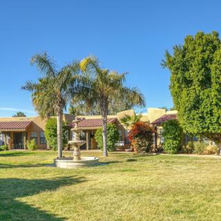A beautiful house with a landscaped garden featuring palm trees and a fountain on a sunny day.